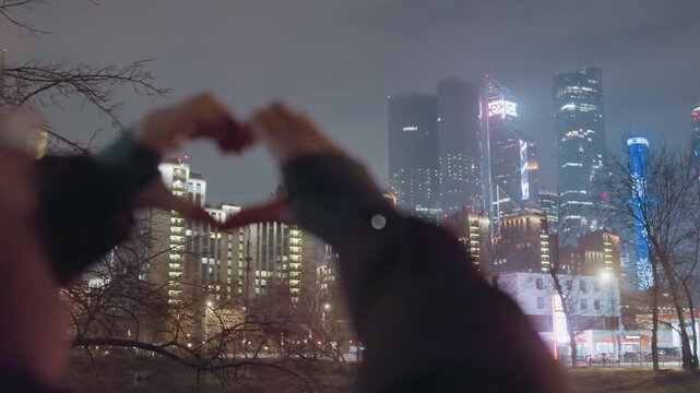 Cityscape heart hands hold tenderness. Silhouette of hands forming affection in city. Intimate hand positioning creating heart shape against city backdrop with blurred lights and soft focus