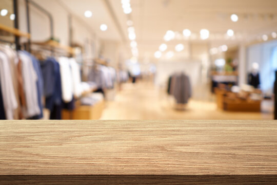 Empty wood table top with blur clothing boutique display interior shopping mall background