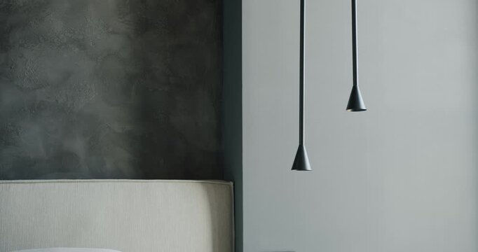 A woman's hand gently interacts with modern pendant lights in a stylish bedroom. The light fixtures hang gracefully against a textured wall, creating a cozy ambiance.