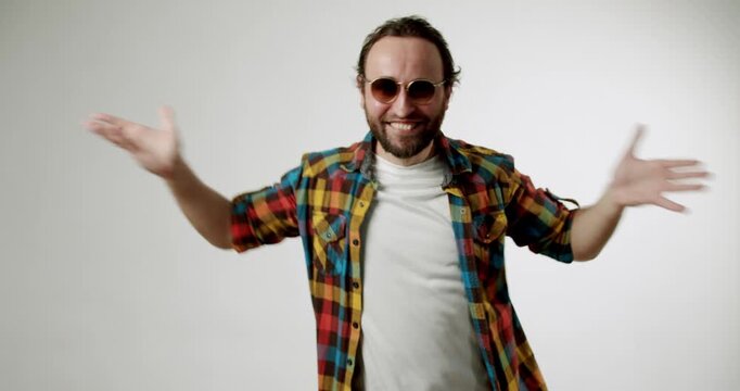 Happy bearded man in sunglasses and colorful shirt dances on white background. He smiles and moves his hands. Joy, fun, and excitement radiate from him. lifestyle and entertainment projects.