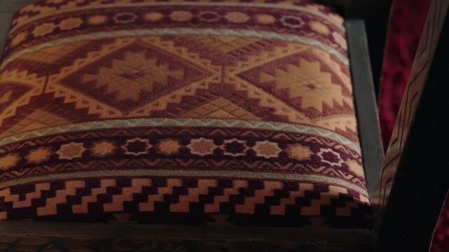 Close-up of an ornate chair cushion with traditional Moroccan patterns and colors. The dark wood frame enhances the rich textures and cultural aesthetic, suitable for travel, interior design,