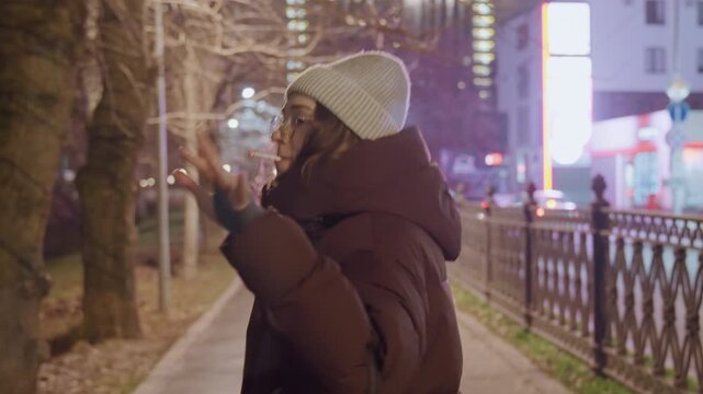 Night sidewalk white woman gesturing, cozy puffer jacket and knit hat, expressive vloggerstyle monologue and street poet performance along park path, candid hand gestures, glasses, winter evening
