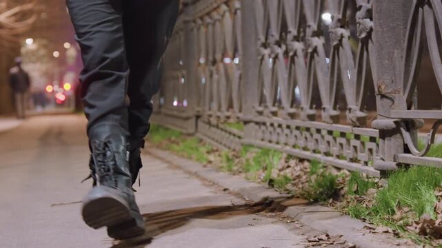 Night sidewalk closeup boots walking along iron railing, damp pavement scuffed by leather laces, quiet urban park path, cinematic lowangle shot, moody atmosphere and reflective shadows.