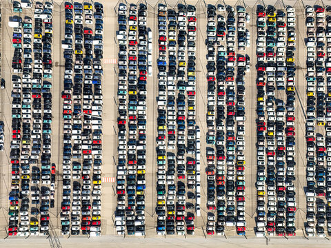 Aerial view of a vast parking lot filled with rows of multi-colored cars parked in neat lines at an industrial facility in Rivalta di Torino, Piedmont, Italy.