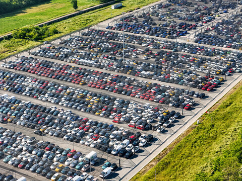 Aerial view of a massive parking lot filled with rows of colorful cars and vehicles next to green fields in Rivalta di Torino, Piedmont, Italy.