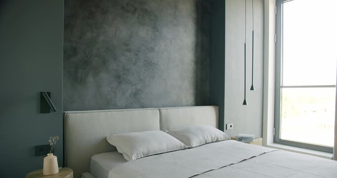 Modern bedroom interior with a large window, textured dark gray walls and a white bed. The room is simple, with a calming and minimalist design.