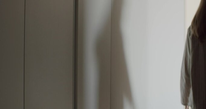 Woman opens a sliding door to a bright room. Getting ready in the morning. New day, new opportunities. Light and airy. Modern apartment. Cozy home. Feeling hopeful. Stepping into the light.