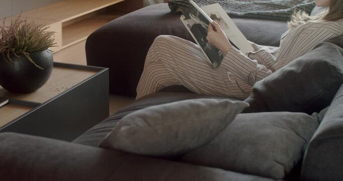 Woman relaxes on comfortable sofa reading magazine. Cozy home living room interior. Calm and peaceful atmosphere. Enjoying leisure time. Serene and tranquil scene. Modern Living Room