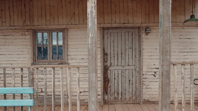 A weathered wooden house stands in a desolate landscape, its paint peeling and a turquoise bench inviting passersby. The scene evokes a sense of solitude and the passage of time,