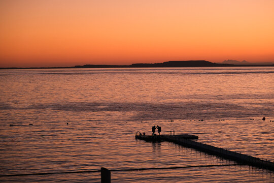 Scuba divers silhouettes standing on the pier in sunset