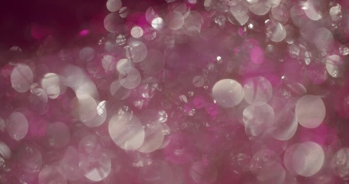 Shiny pink and white glitter particles creating a shimmering bokeh effect while moving and sparkling against a dark background, making a beautiful abstract and festive macro shot