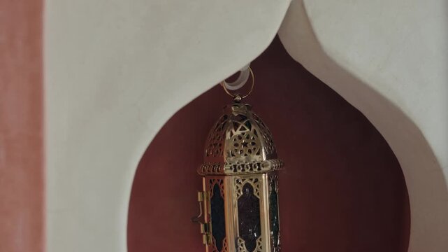 Ornate brass lantern hanging in a Moroccan alcove. This traditional lamp is perfect for adding a touch of elegance to any space. It is ideal for use in homes, hotels, or restaurants.