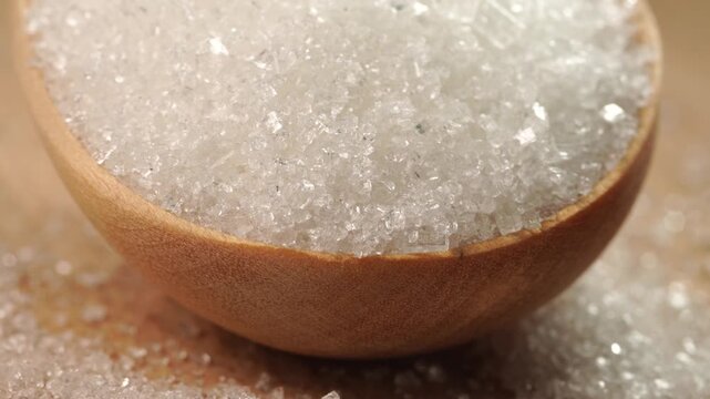 White granulated sugar on a wooden spoon slowly turning, close-up, macro.
