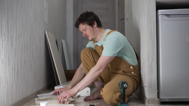 Young man in overalls experiencing frustration and failure while trying to assemble new furniture, feeling overwhelmed by complicated instructions and the difficulty of the diy project