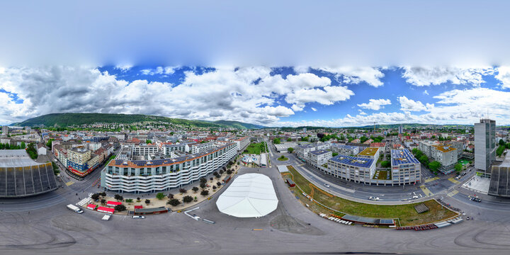 Aerial view of modern urban architecture, a large white event tent in a central square, and surrounding hills under a cloudy sky in Biel/Bienne, Canton of Bern, Switzerland.