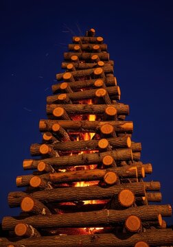 Dry logs stacked high for a massive bonfire, showing the textured wood ready to ignite quickly and burn intensely under the night sky, flammable, preparation, energy