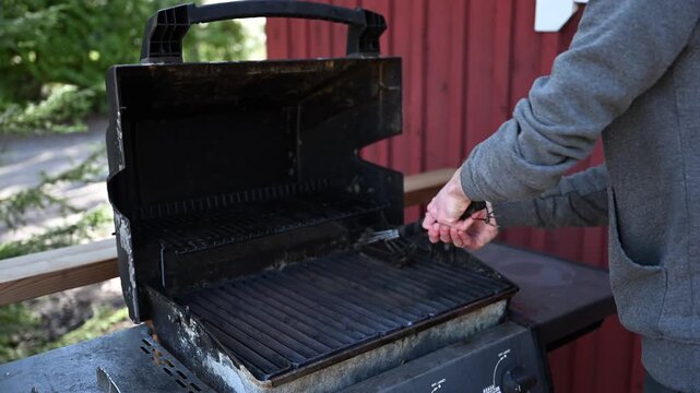 Cleaning outdoor barbecue grill with wire brush on wooden terrace in summer cottage backyard