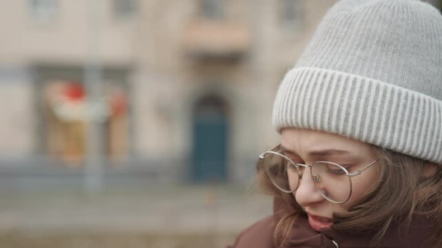 Caucasian woman student startled by phone in park, close reaction, winter coat and beanie, glasses fogged, scrolling through messages, concerned expression and quick phone call, candid street portrait