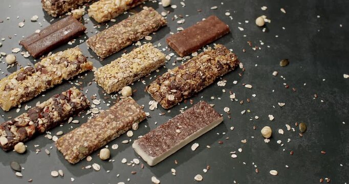 Assorted granola bars and healthy snacks arranged on a dark surface with scattered seeds and nuts. Nutritious food concept, ideal for promoting healthy eating and snack options. Granola Bars