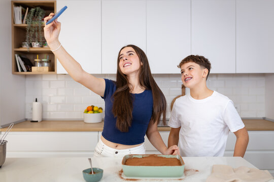 Siblings baking cake taking a happy selfie in kitchen