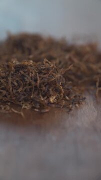 Primer plano vertical de tabaco suelto picado sobre mesa de madera r&uacute;stica con fondo desenfocado y luz natural.