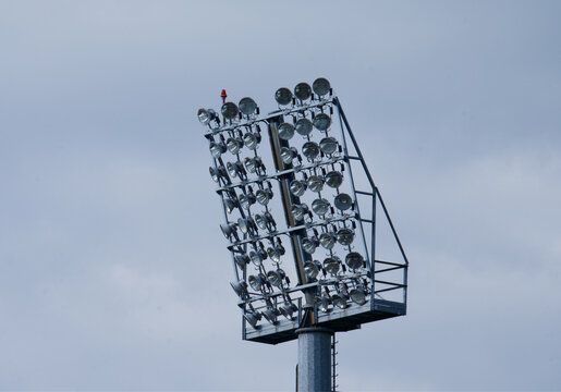 High stadium lighting mast with powerful floodlights against a cloudy sky.