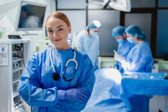 Close up portrait of female anesthesiologist without mask in operating theater, confident expression, sterile medical clothing, blurred surgeons working in background, healthcare and surgery concept