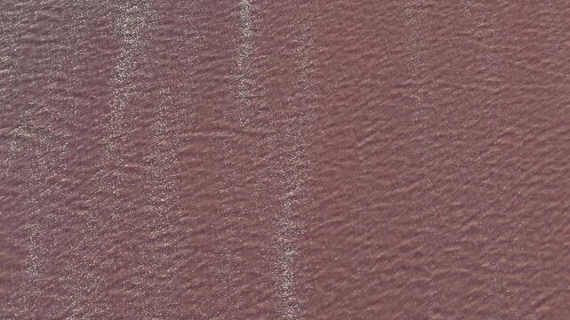 Drone aerial view of pink salt lake water texture with shimmering ripples in Laguna Rosa Torrevieja, Spain.