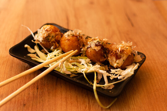 takoyaki balls on black plate with chopsticks on wooden table