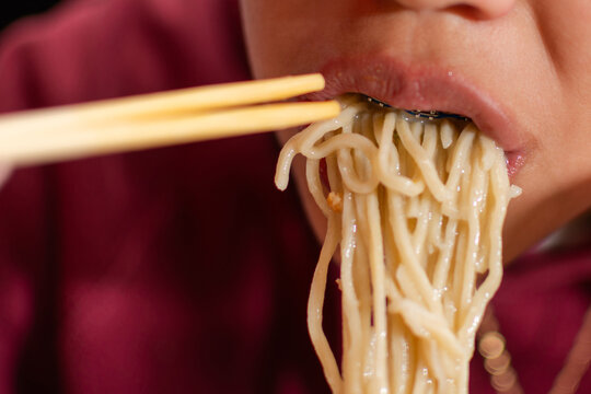 Close up of young person eating ramen noodles with chopsticks