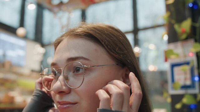Caucasian woman securing elegant bun with hairpin in warm indoor space, glasses framing face, hands working nape, string lights and soft bokeh, focused meticulous movement, quiet creative preparation