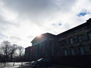 Obraz premium Sunlit neoclassical National Galleries Scotland, Modern One building facade with parked car and bare trees in Edinburgh, Scotland, UK under a dramatic cloudy sky