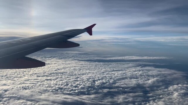 An aerial view of a blue jet airplane in flight, soaring high above the clouds and earth&rsquo;s horizon as the aircraft wings glide through the sky during a travel trip