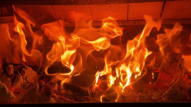  Slow motion handheld close-up of intense roaring flames in a fireplace. Cinematic shot of large, bright orange fire burning wood logs in a hearth. Warm and powerful atmosphere background