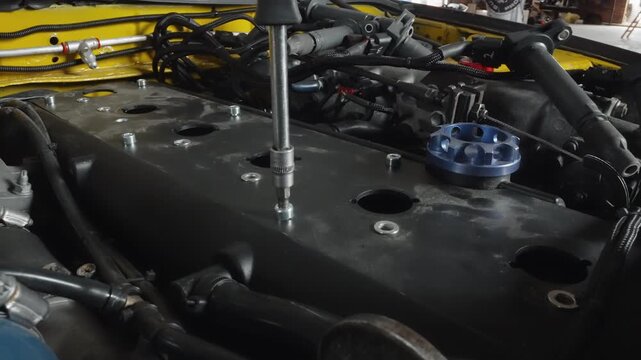 Closeup black engine cover blue cap hoses, yellow chassis background, bolt holes and wiring visible, workshop lighting, technical repair and tuning, diagnostic inspection and parts layout