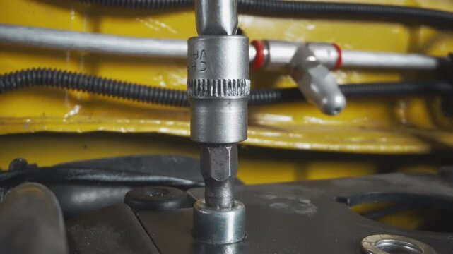 Closeup socket driver tightening engine bolt, socket engaged on nut, rotating ratchet, checking torque, yellow chassis background, metal surfaces and wiring, pneumatic tool nearby, precision fastening