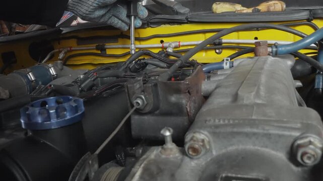 Worn engine undergoing restoration with scattered repair equipment inside vehicle. Detailed image of rusted engine area being fixed with oil and multiple repair instruments inside vehicle compartment