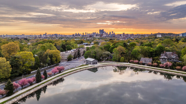 Aerial view of Brookline Reservoir surrounded by blooming cherry blossoms and lush greenery with the Boston skyline at sunrise in Brookline, Massachusetts, United States.