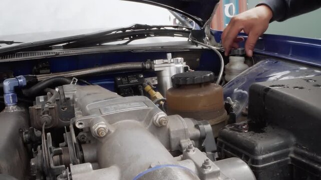 Closeup mechanic hands checking reservoir engine bay blue car hood open, focus on reservoir cap, hoses, intake manifold, careful tightening, instructional maintenance, daylight workshop atmosphere,