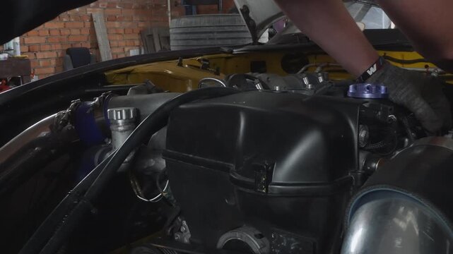 Gloved hands inspecting engine sensor hoses, focused tech measures pressure and tightens clamps inside clean garage bay, closeup on braided lines, aluminum fittings, wires and connectors, careful