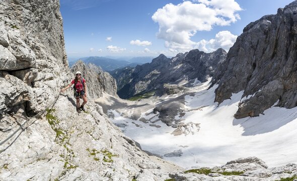 Mountaineer with helmet in a secured via ferrata, Zugspitz via ferrata, ascent to the Zugspitze, view of mountain basin with snowfield of the H&ouml;llentalferner and H&ouml;llental, Wetterstein range, Bavaria, Germany