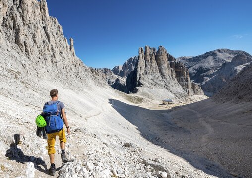Hiker descending from the Santner via ferrata to the Gartl hut, Rifugio Re Alberto, at the back climbing cliffs, Vajolett towers, Rosengarten group, Dolomites, South Tyrol, Trentino-Alto Adige, Italy