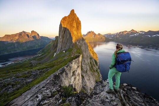 Hiker looks at landscape, evening mood, steep mountain Segla, fjord Mefjorden with mountains, island Senja, Troms, Norway