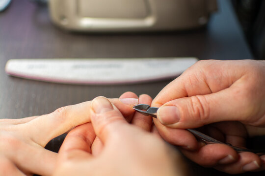 A manicurist uses cuticle scissors to remove cuticles from nails for a manicure at a beauty salon.