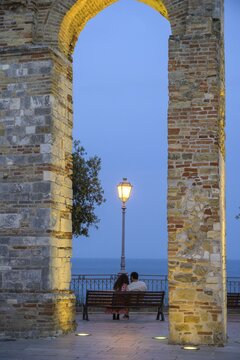 Old archway at the Belvedere and a couple sitting on a bench looking at the sea, Numana, province of Ancona, Italy