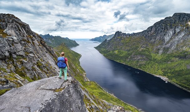 Fjord and mountains, view from mountain Barden, young hiker standing at a cliff, Senja, Norway