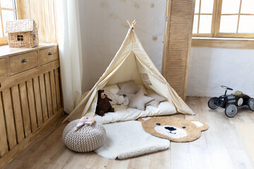 Cozy Scandinavian style children room interior with indoor teepee tent, soft pillows, natural decor. modern nursery playroom with toys for kids. Stylish family home interior with hygge atmosphere. © stock_studio
