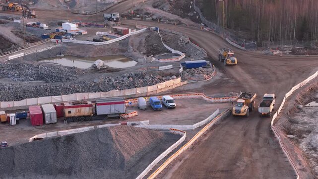 Espoo, Finland-April 14, 2025: Several trucks are driving on a dirt road within a crushed stone production area in Finland, with containers, puddles, and a temporary fence visible in the background