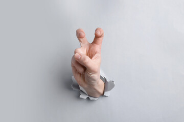 Naklejka premium Woman showing air quotes with fingers through hole in grey paper, closeup