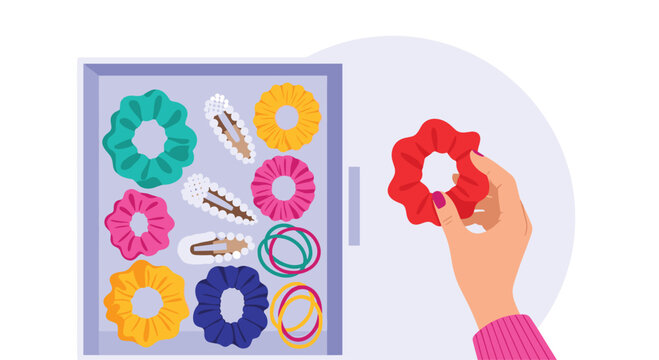 A hand selects a vibrant red scrunchie from a drawer filled with an assortment of colorful hair accessories and pearl-adorned clips for styling.
